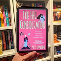 a woman holding a book for her consideration in front of a bookshelf